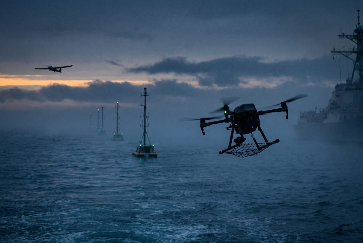 A line of slender sensor masts rising from coastal water at dusk, with a small four-rotor interceptor climbing hard in the foreground toward a distant hostile drone, and the softened grey side of a warship in the haze behind.